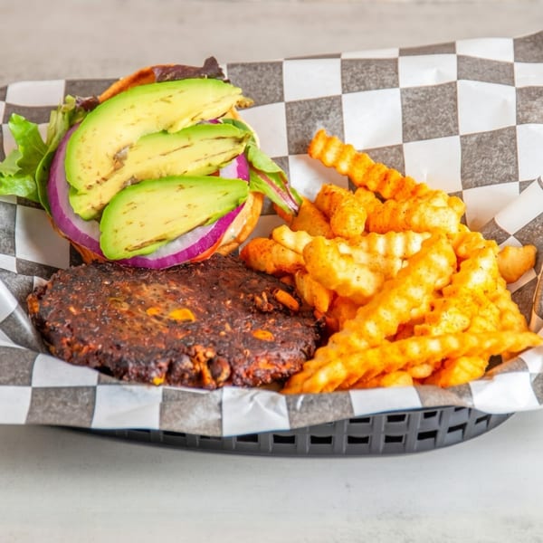 A black bean burger with avocado, red onion, and lettuce, served with crinkle-cut fries.
