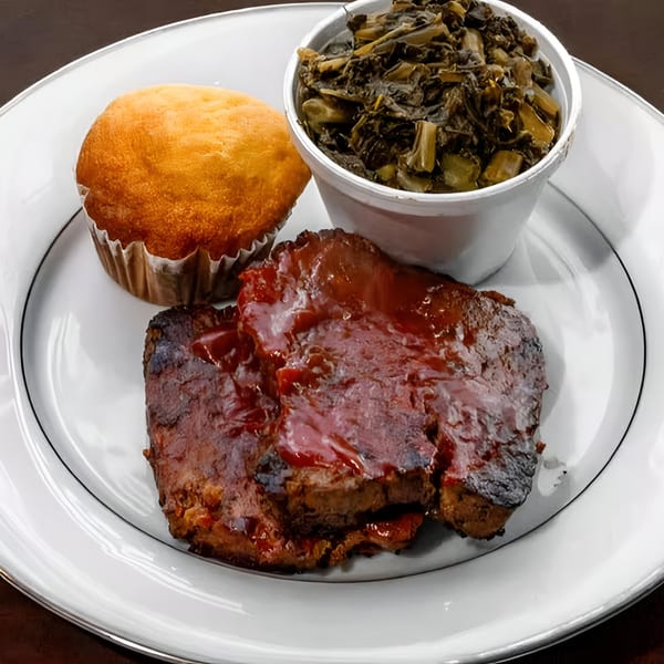 Southern-style meal with BBQ meat, a corn muffin, and a side of collard greens.