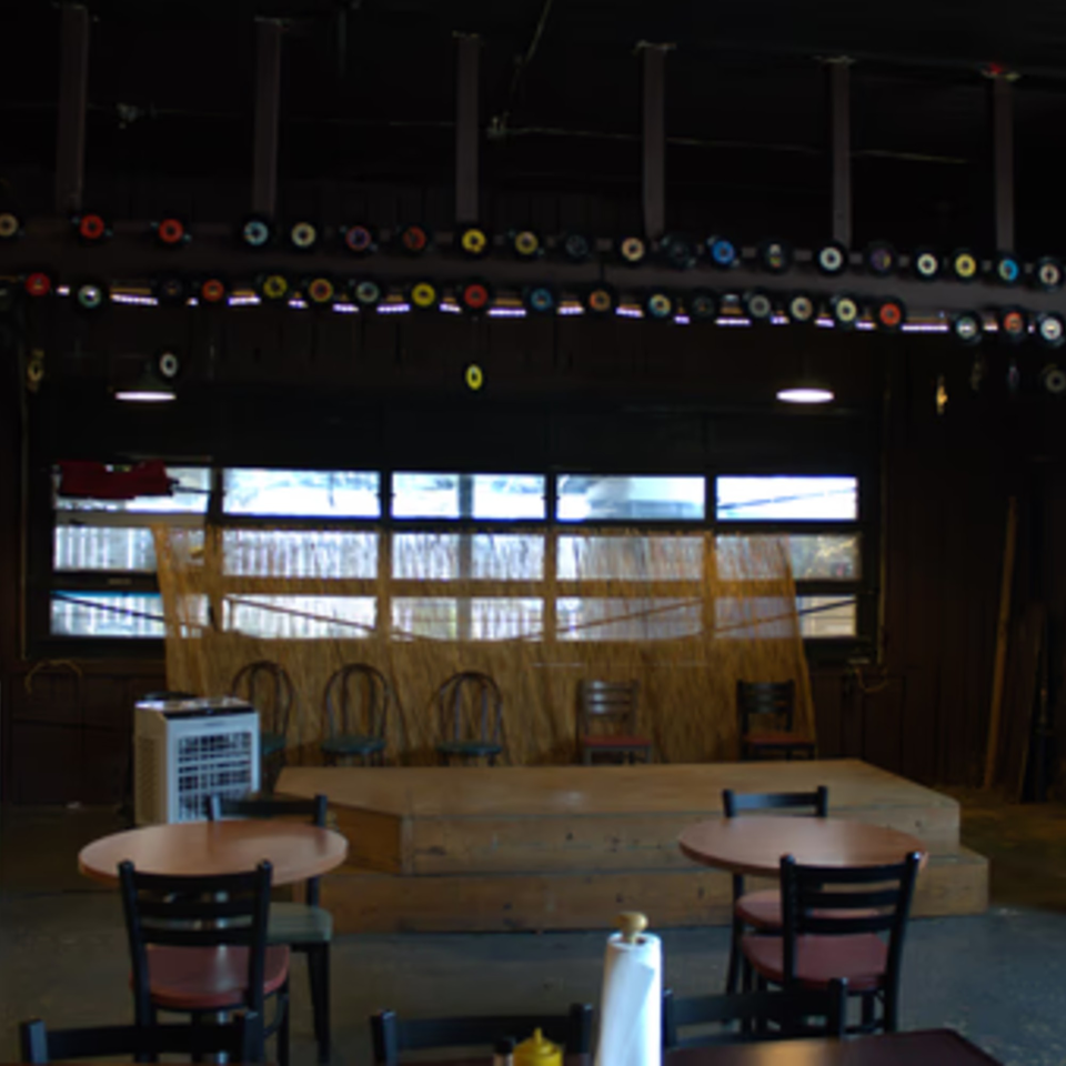 The Service Station Restaurant's interior with a stage, tables, chairs, and record decorations.