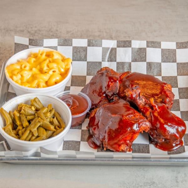BBQ chicken, mac and cheese, green beans, and a side of sauce on a checkered paper.