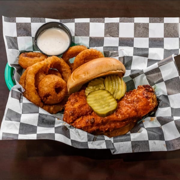 Southern fried chicken sandwich with pickles and onion rings, served in a basket with ranch.