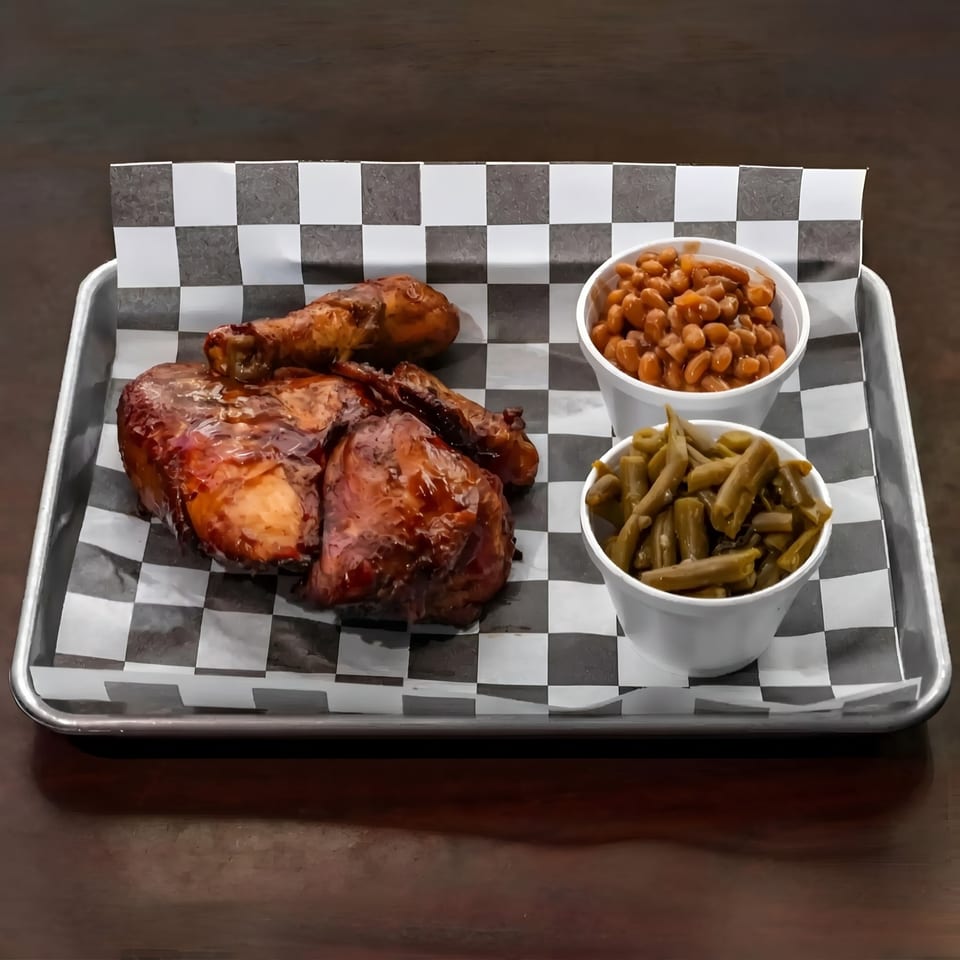 BBQ chicken with baked beans and green beans on a checkered paper-lined tray.