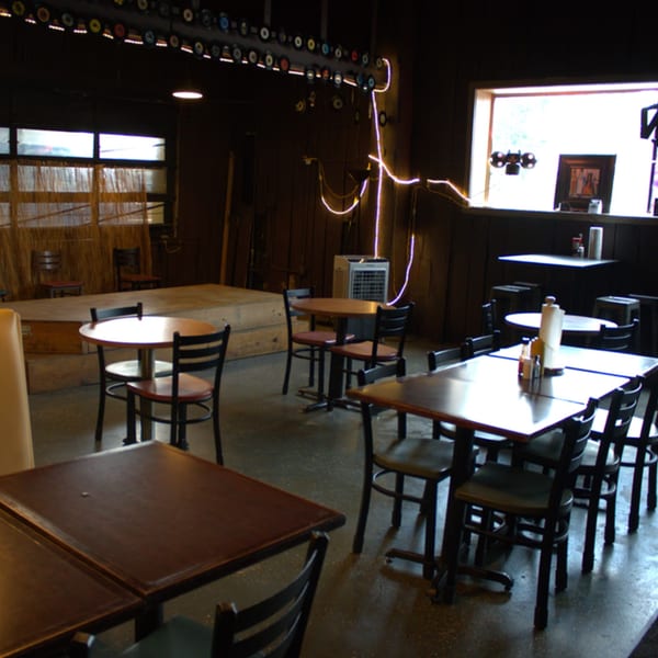 Interior of The Service Station Restaurant, with tables, chairs, a stage, and neon lighting.
