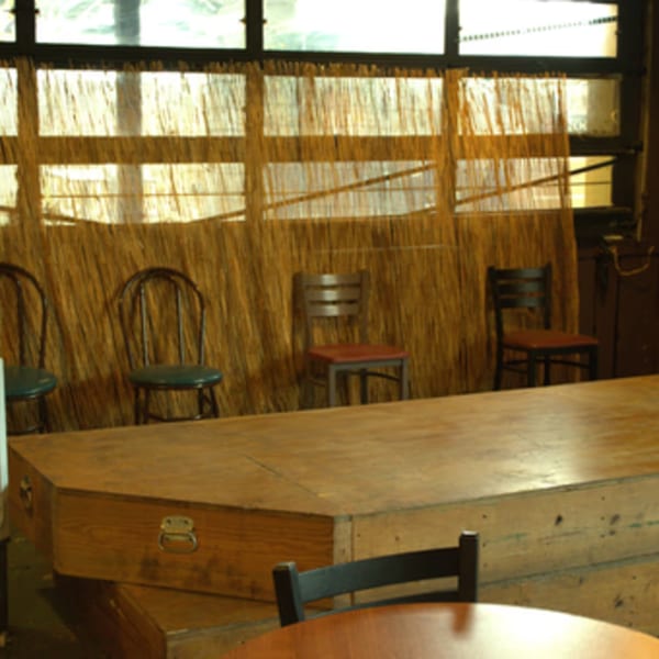 Empty chairs and wooden boxes against a wall with straw-like coverings and windows.